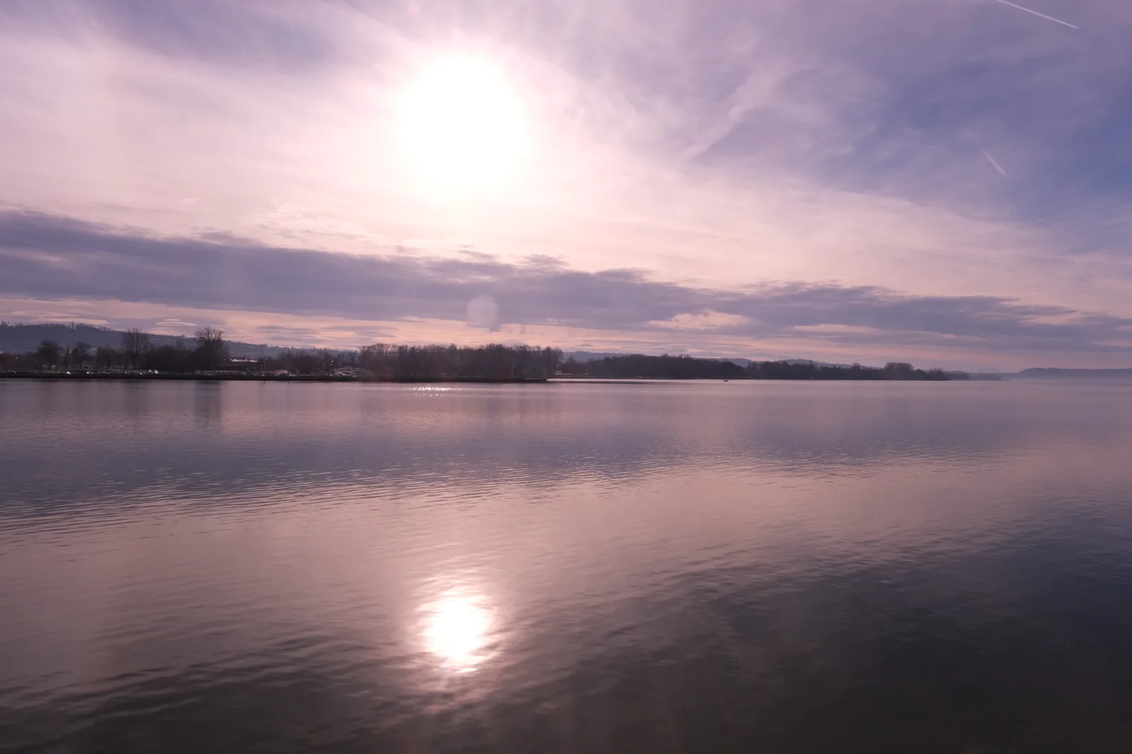 Sonnenlicht spiegelt sich auf einer weiten Wasserfläche unter violett schimmerndem Himmel.