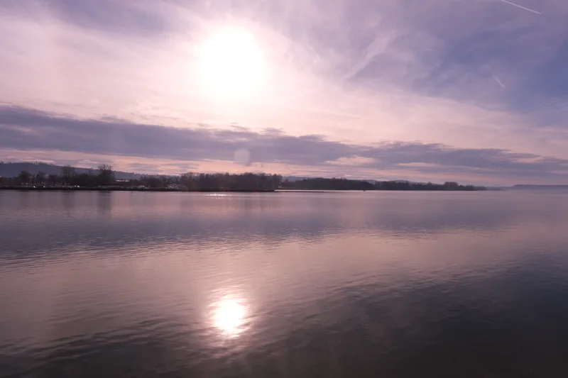 Sonnenlicht spiegelt sich auf einem See unter violett schimmerndem Himmel.