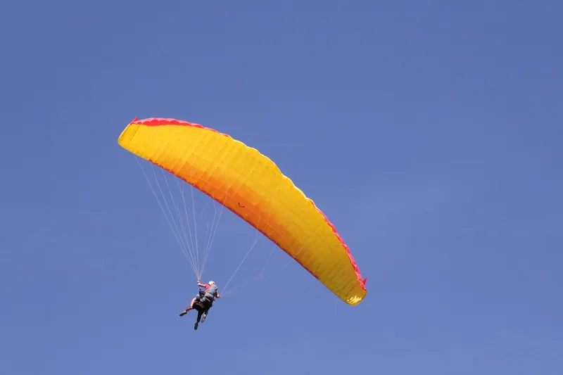 Ein Gleitschirm mit gelbem Schirm schwebt vor blauem Himmel.