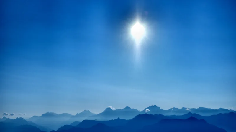Die helle Sonne steht über mehreren blauen Bergketten.
