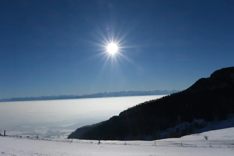 Sonnenschein über einer verschneiten Landschaft und einem weiten Nebelmeer.