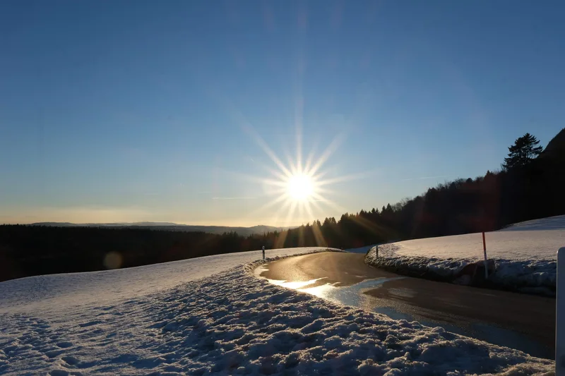 Tief stehende Sonne über einem verschneiten Ufer und einer Wasserfläche.