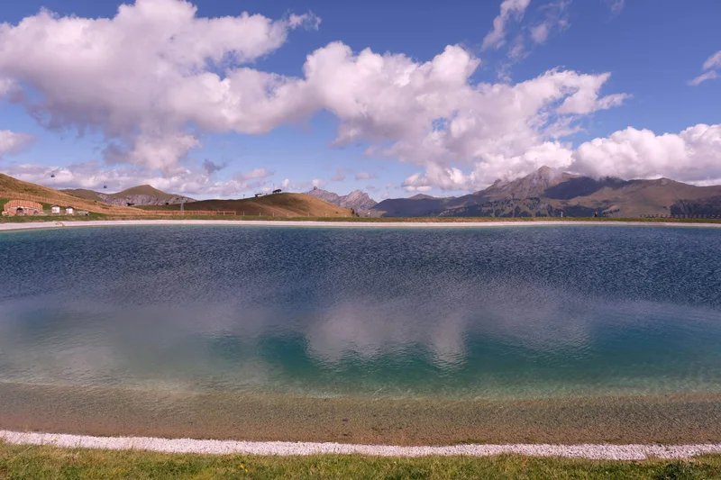 Türkisblaues Wasser eines Bergsees unter hellen Wolken und Berggipfeln.
