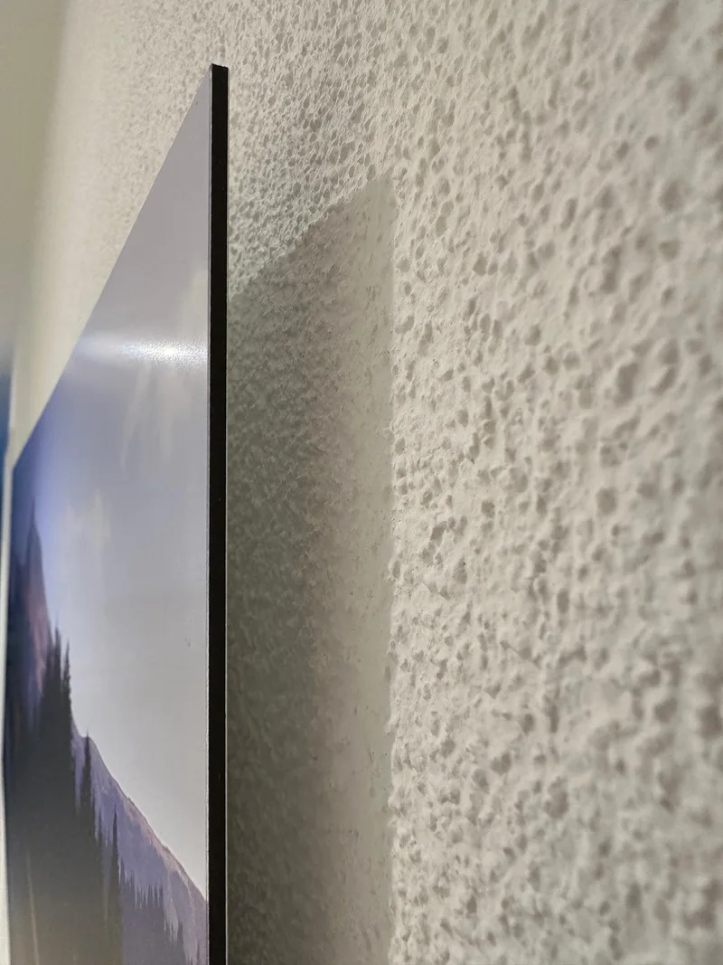 Nahaufnahme der dünnen dunklen Bildkante und des Abstands zwischen dem Dibond-Bild und der Wand.