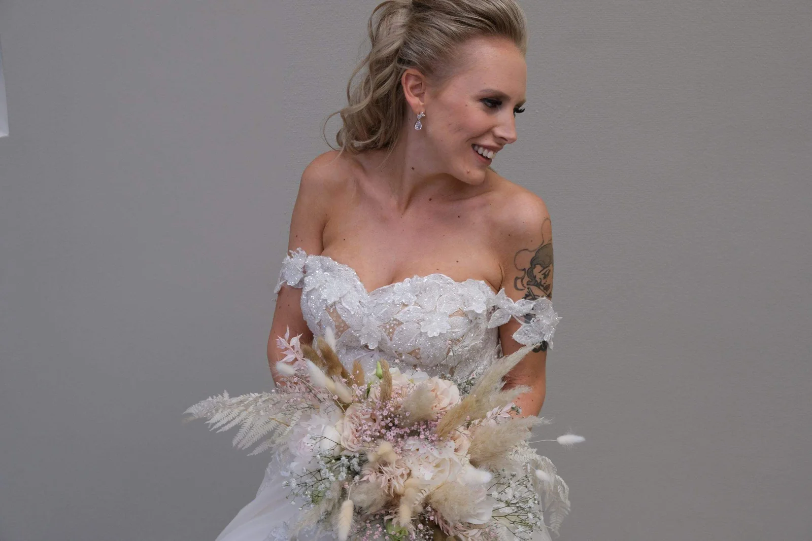 Eine lächelnde Braut mit Blumenstrauss, vor einem ruhigen grauen Hintergrund fotografiert.