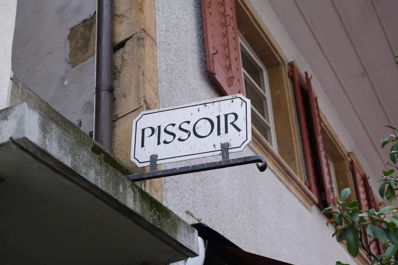 Ein altes Schild mit der Aufschrift Pissoir an einer Hausfassade.
