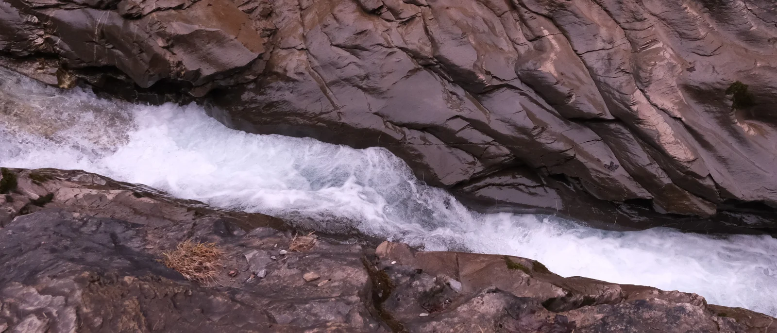 Weisses Wasser fliesst zwischen dunklen, von der Strömung geformten Felsen.